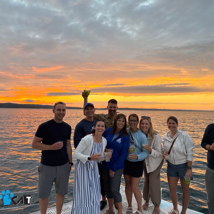 Group of people smiling on a boat at sunset with an orange-lit sky.