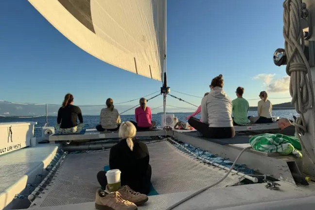 People performing yoga on a sailboat at sea during sunset.